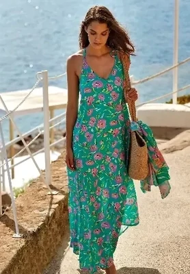 Roidal Tessy Blume Sonia Maxi Dress. A flowing sun dress in a colourful fabric of turquoise sea green liberally scattered with pretty pink Tahitian flowers. Lifestyle photo,