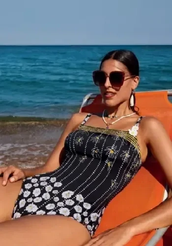 Magda Shaper Swimsuit by Nuria Ferrer. The black suit features stylised drawings daisies joined by chains of dots, and some of the pretty golden yellow daisy centres are softly heart shaped. Lifestyle photo.
