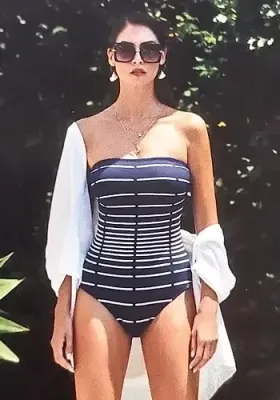 Capri Hourglass Illusion Bandeau Swimsuit by Nuria Ferrer. The fabric is a navy blue with a patter in white giving the illusion of a narrow waist. Lifestyle photo.