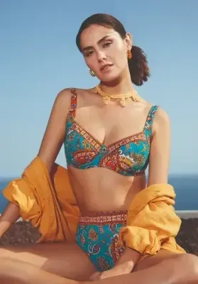 Nuria Ferrer Ornela Underwired Shaper Bikini. The top is supported by underwired fabric lined cups. The shoulder straps are adjustable. The matching bikini pants have a shaping and smoothing effect giving good coverage. The fabric is a Blue Paisley print. Lifestyle photo