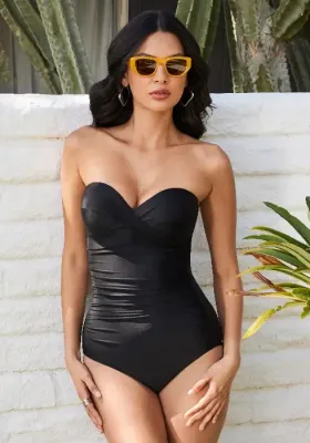 Madrid Black Bandeau Swimsuit by Miraclesuit. A classic bandeau style swimsuit with the addition of completely removable shoulder straps. Lifestyle photo with model wearing sunglasses.