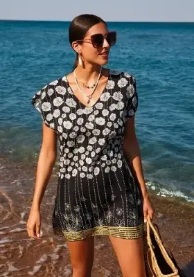 Magda Tunic Dress by Nuria Ferrer Magda Tunic Dress by Nuria Ferrer. The Magda tunic dress features a V-neckline, and short sleeves . The fabric is a white daisy on a black background. Lifestyle photo.