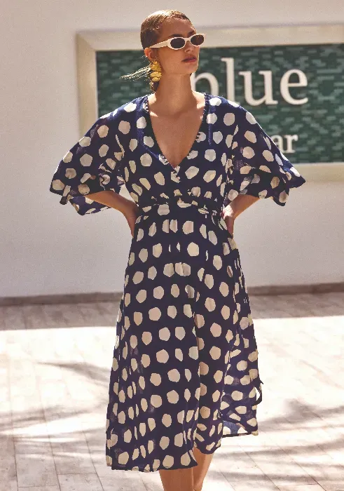 Lifestyle photo of David Polka Dots Midi length Dress. The fabric is white asymmetric dots on a navy blue background