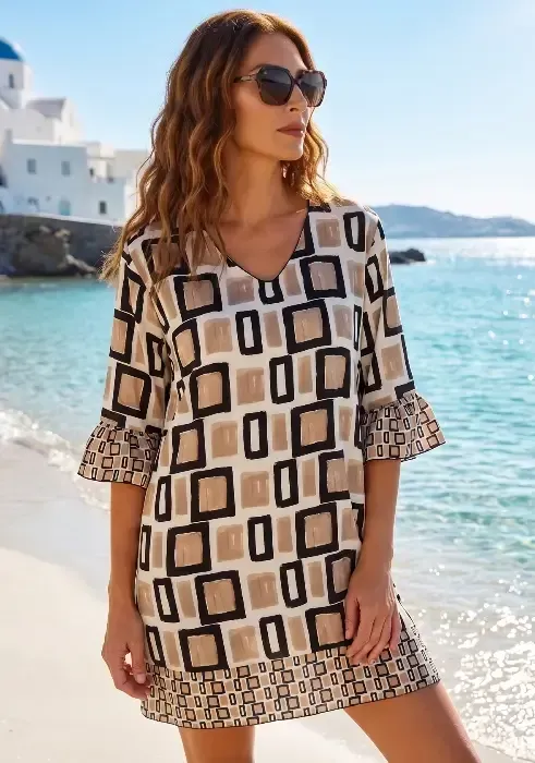 A model on a beach wearing a Nuria Ferrer Geo Short Kaftan Dress in a brown, white and black geometric design. 