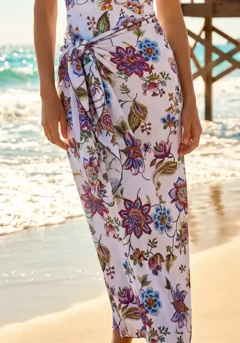 Jasmine Pareo by Nuria Ferrer Close up of a model wearing a Jasmine Pareo by Nuria Ferrer. The fabric features colourful flowers on a white background.