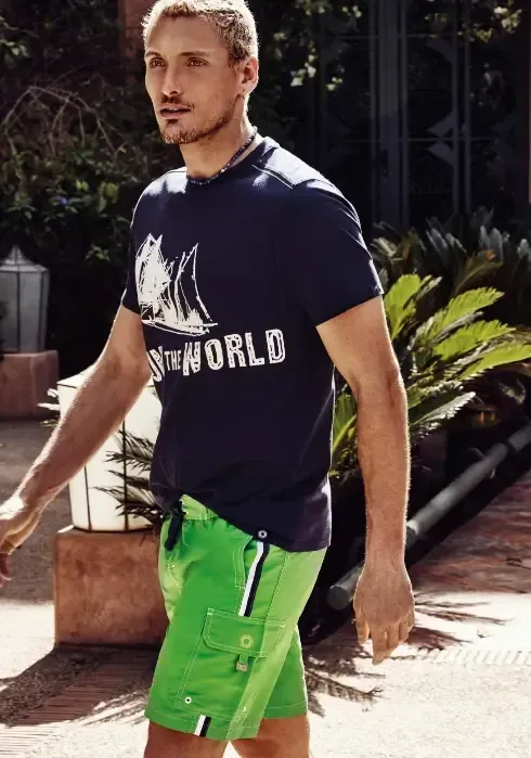 Lifestyle photo of Adventure Cargo Swim Shorts. Green swimshort with thin black &  white side stripes and pockets 