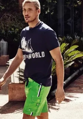 Lifestyle photo of Adventure Cargo Swim Shorts. Green swimshort with thin black &  white side stripes and pockets 