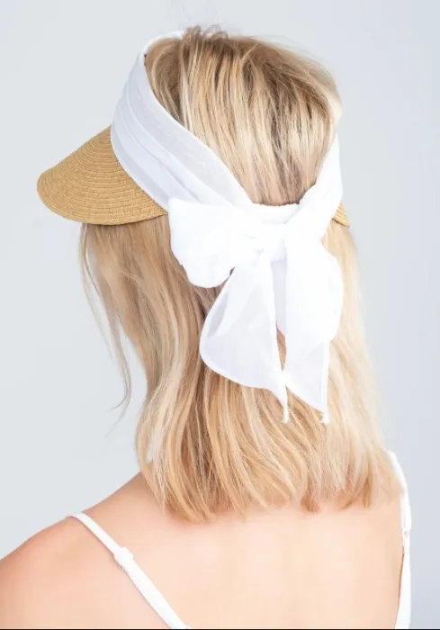 Lifestyle photo of Misha Visor in natural woven tone with white material band that can be tied into a bow to fasten.