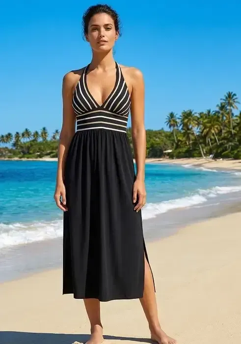 A woman poses on a beach wearing a Nuria Ferrer Atena midi dress with a striped halter bodice and black flowing skirt.
