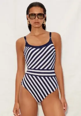 Elora Scoop Neck Comfort Swimsuit A woman models a Nuria Ferrer one-piece swimsuit with navy and white diagonal stripes, a scoop neck, and gold strap accents.