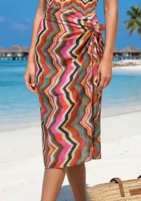 Miranda Pareo by Nuria Ferrer A model wears a colourful chevron-print sarong tied at the waist on a sunny tropical beach with matching swimsuit.