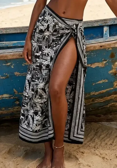 Woman wearing a black and white tropical print Nuria Ferrer Bahia pareo wrap skirt on a beach by a blue boat.