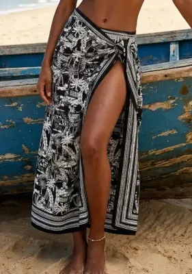 Woman wearing a black and white tropical print Nuria Ferrer Bahia pareo wrap skirt on a beach by a blue boat.