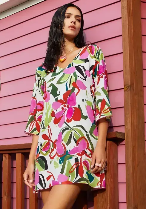 A model wearing a Nuria Ferrer Hana Sun Dress stands outside of a building. The fabric is a multicoloured floral print.