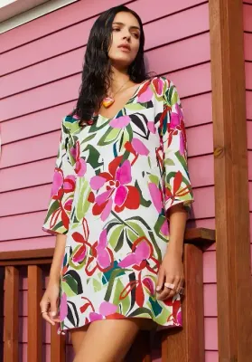 A model wearing a Nuria Ferrer Hana Sun Dress stands outside of a building. The fabric is a multicoloured floral print.