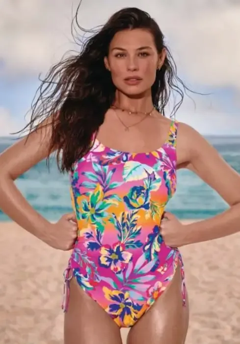 Woman on a beach wearing a vibrant pink & orange Rosa Faia Jesse Beauty-full Comfy F cup swimsuit with bright floral pattern