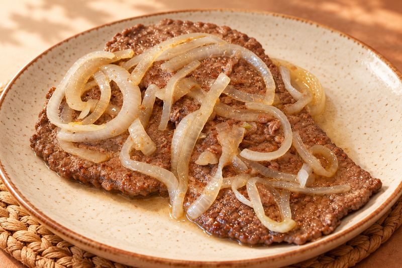 Bistec encebollado con aros de cebolla en plato de cerámica