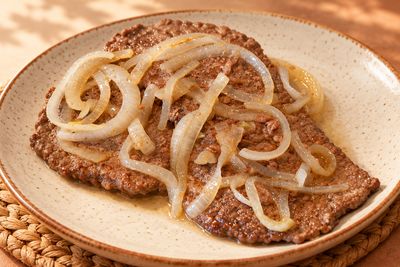 Bistec encebollado con aros de cebolla en plato de cerámica