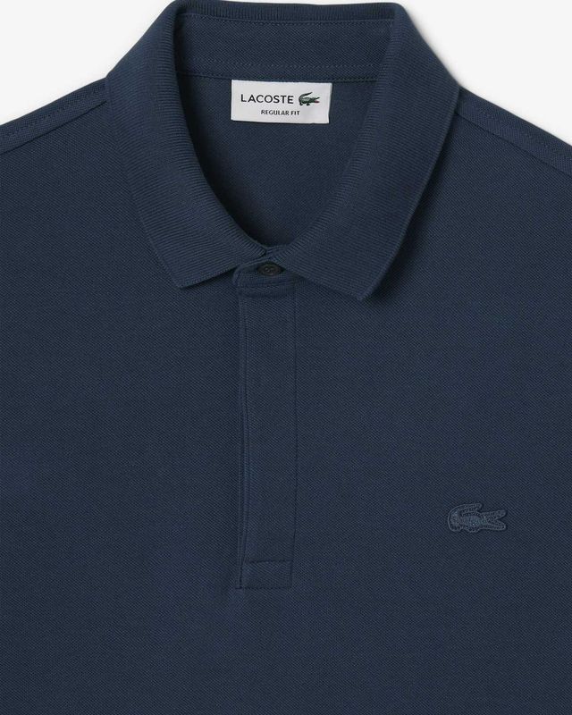 Detail van de Lacoste Paris polo in azuurblauw met ton-sur-ton logo en verborgen sluiting

