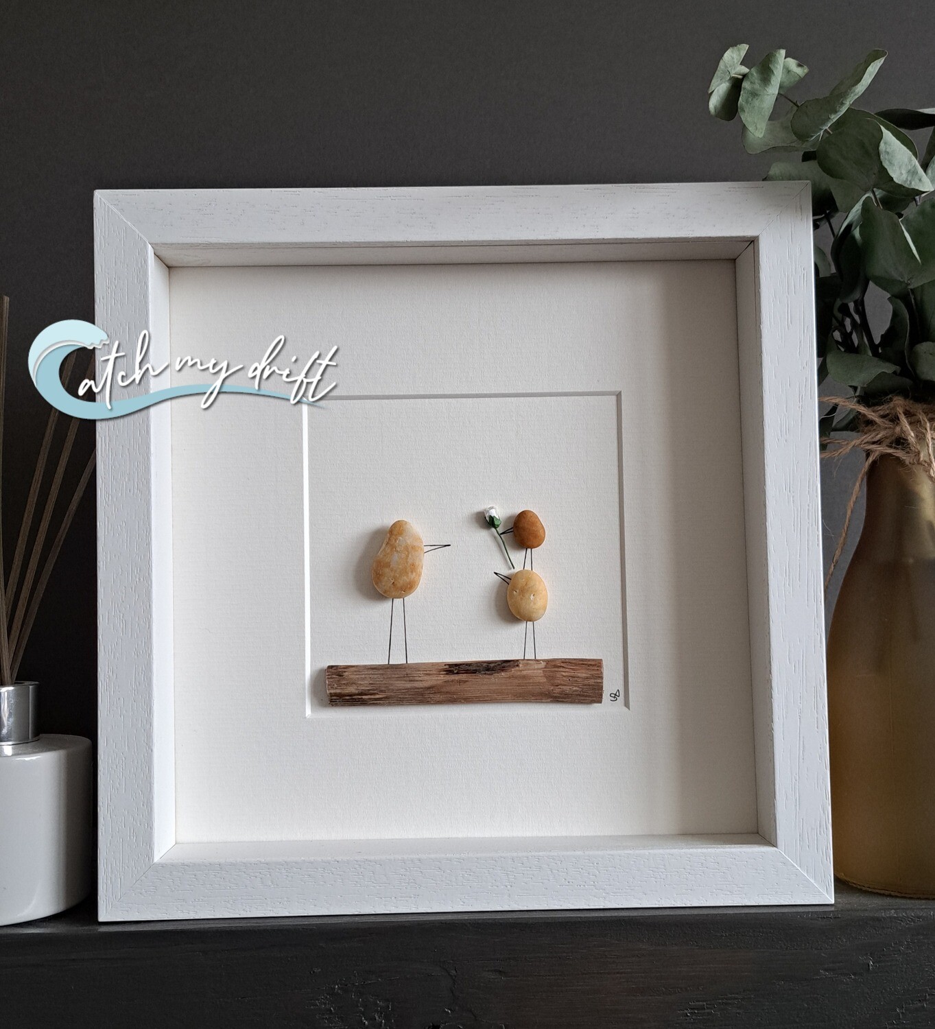 2 golden pebble bird children, one on top of the other presenting a rose to adult pebble bird all on a wooden perch 