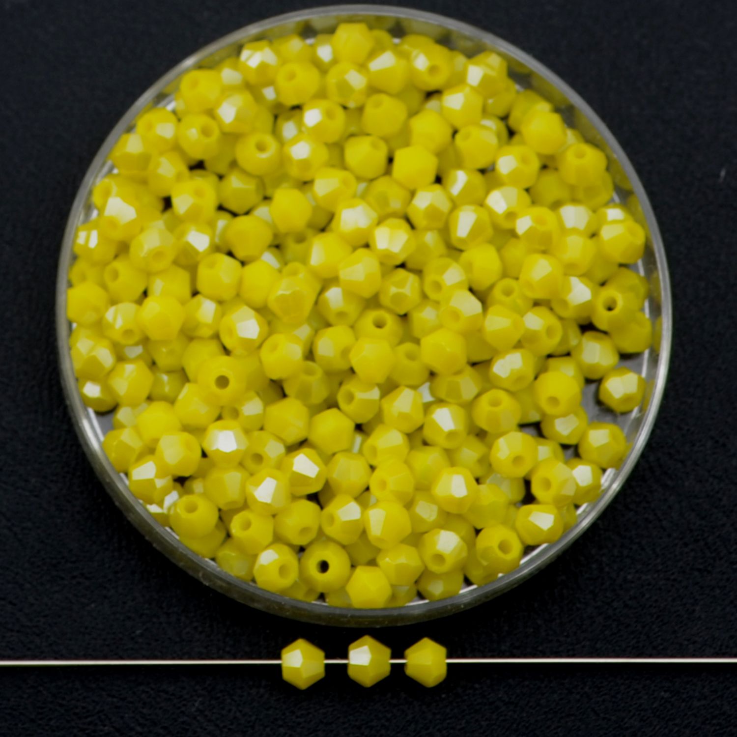 Facettierte Glasperlen in kräftigem Gelb, Bicone-Schliff, 3 mm, auf schwarzem Hintergrund