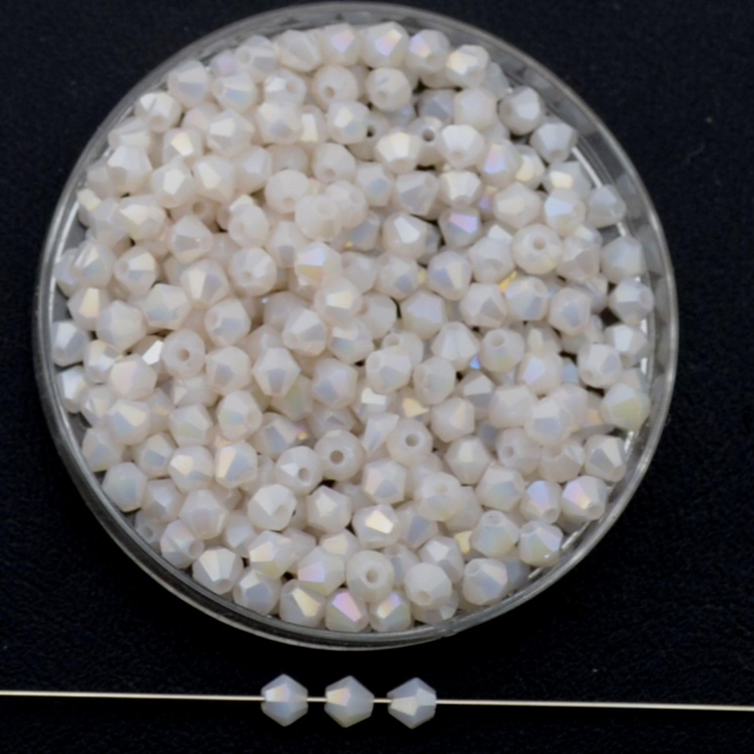 Facettierte Glasperlen in Roséweiß, Bicone-Schliff, 3 mm, mit feinem AB-Schimmer auf schwarzem Hintergrund