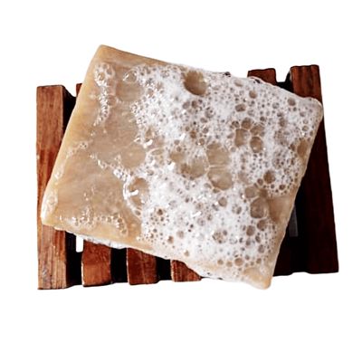 A lathered brown soap bar with visible suds sitting on a slatted wooden soap dish.
