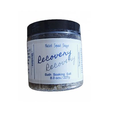 A clear jar with a black lid and a white wraparound label, displaying brown crystals inside.