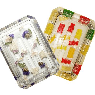 A pair of clear resin dishes—one embedded with delicate purple flowers, and the other with colorful gummy bears in various shades.