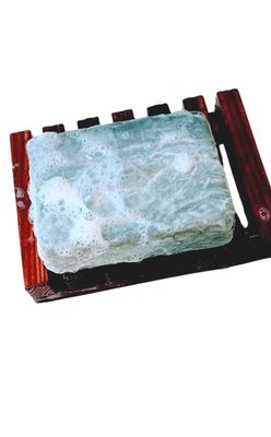 A lathered gray and white soap bar placed on a slatted wooden soap dish.