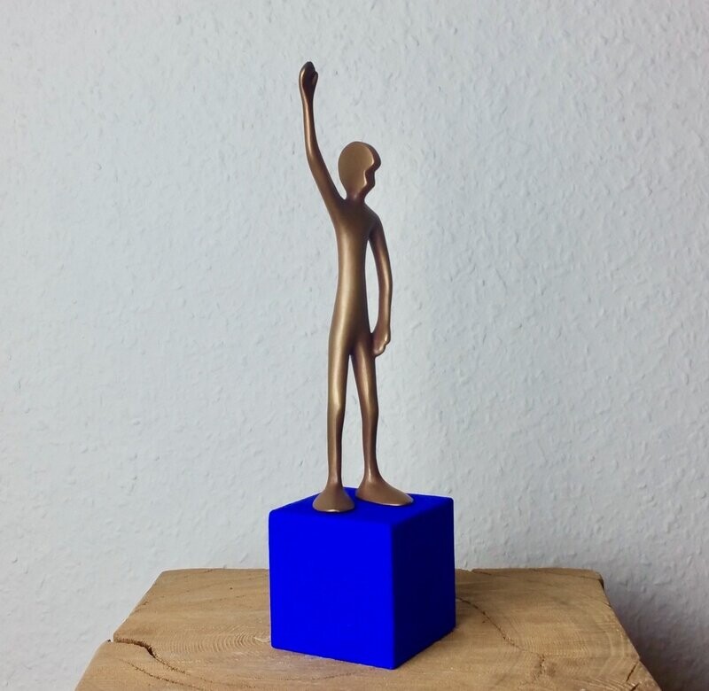Das Bild zeigt  die Bronzeskulptur "Kleiner winkender Friend mit blauem Sockel" von Bildhauer Oliver Pohl aus Haste.