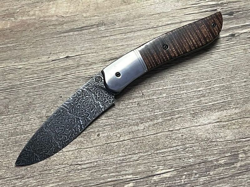 Couteau Névé von Tim Bernard (Flipper), Griff Koa-Holz cross cut, Mitres hochglanz, Gürtelclip, Klinge 300 Lagen Mosaikdamast Couteau Névé von Tim Bernard (Flipper), Griff Koa-Holz cross cut, Mitres hochglanz, Gürtelclip, Klinge 300 Lagen Mosaikdamast