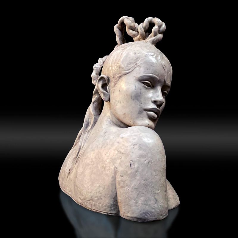 Busto de piedra gris de una mujer con una trenza sobre la cabeza, apoyando la barbilla en el hombro, mira a la derecha y se ve su espalda