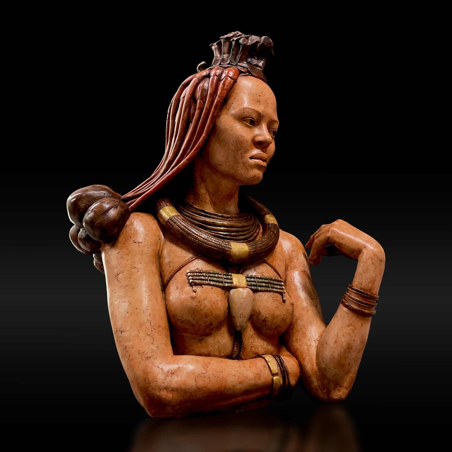 Escultura de un busto de una mujer Himba con un brazo cruzado bajo el pecho y una mano apuntando hacia sí misma con actitud relajada y reflexiva mirando hacia nuestra derecha