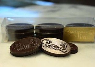 Our oval wafers infused with peppermint decorated with our logo on top.  Behind the chocolates is a box with 9 wafers