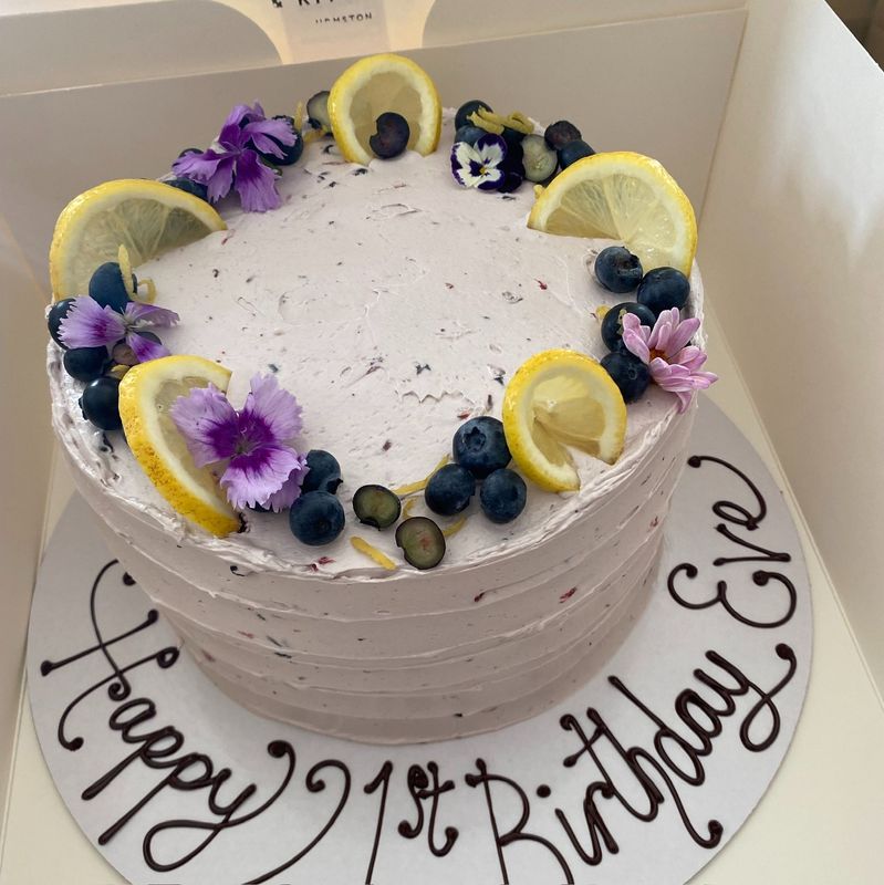Lemon and Blueberry Cake - Lemon and blueberry sponge layered with tangy lemon curd and finished with a blueberry Swiss meringue buttercream. Topped with fresh blueberries, lemon slices, and edible flowers for a vibrant and elegant look.