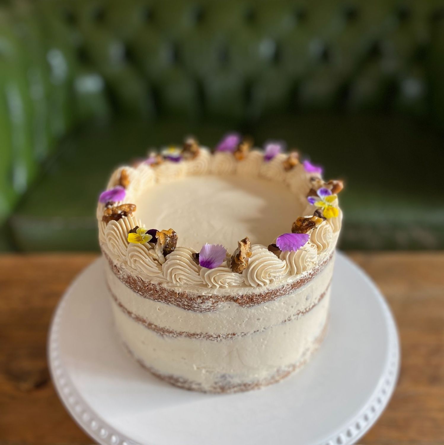 Coffee & Walnut Cake - A rich and nutty classic with a bold KIN twist. Three layers of espresso-soaked sponge with toasted walnuts throughout, filled and iced with smooth espresso Swiss meringue buttercream. Finished with golden walnut brittle, roasted coffee beans, and edible flowers for a touch of elegance — this one’s a must for coffee lovers.