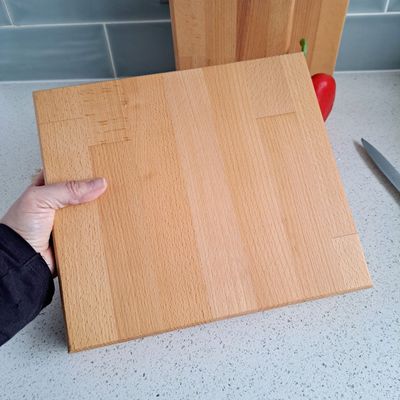 Large beech chopping board A hand holding up a light wood chopping board. In the background you can see part of another chopping board and a red pepper