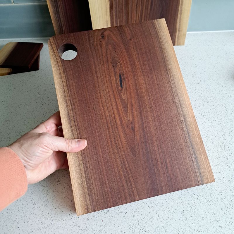 Walnut chopping board No.5 A hand holding a dark wooden chopping board with light edges. The board is made out of American black walnut.