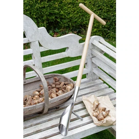 Long handled Garden Bulb Planter set against a white garden bench and wooden trug with bulbs in.