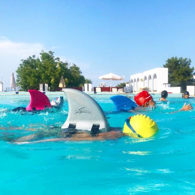 Image of child in yellow swim hat and grey swimfin, swimming in swimming pool