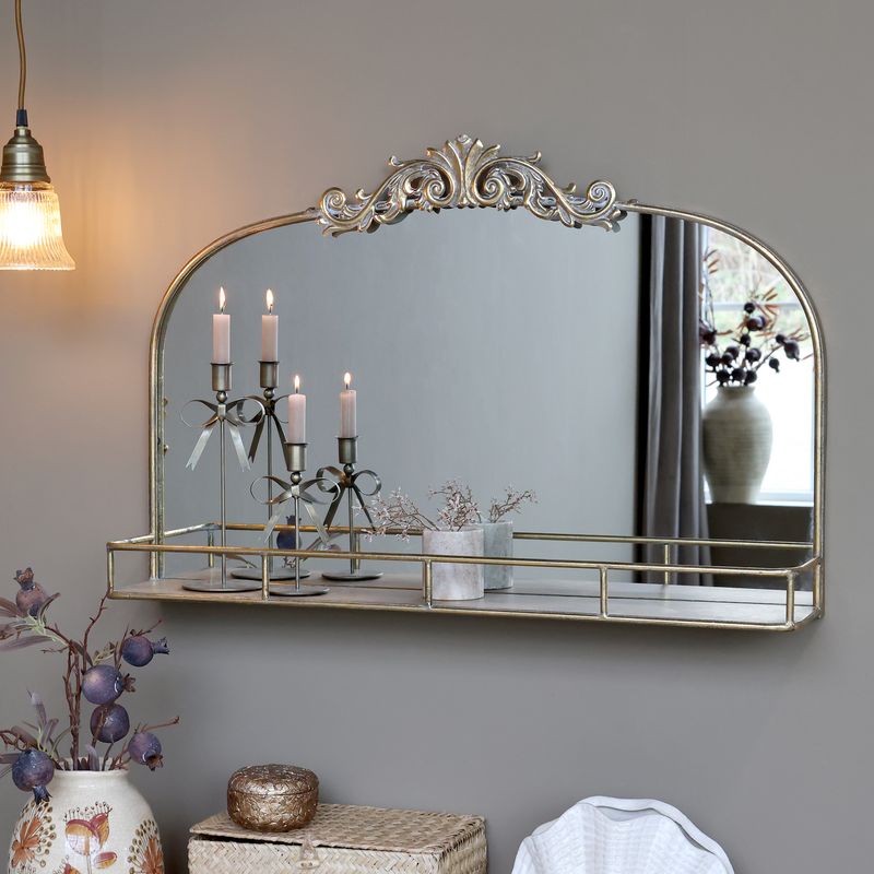 Antique-style arched wall mirror with decorative metal crest and integrated narrow shelf in a vintage brass finish.