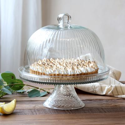 Clear glass cake stand with ribbed dome lid, round platter, and decorative pedestal base.