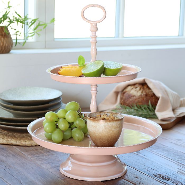 Two-tier rose-coloured metal étagère with round trays, a turned central stem, and a decorative ring handle on top.