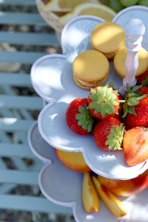 Two-tier white ceramic serving stand holding grapes and sliced fruit, styled on a rustic kitchen table with bread and plates