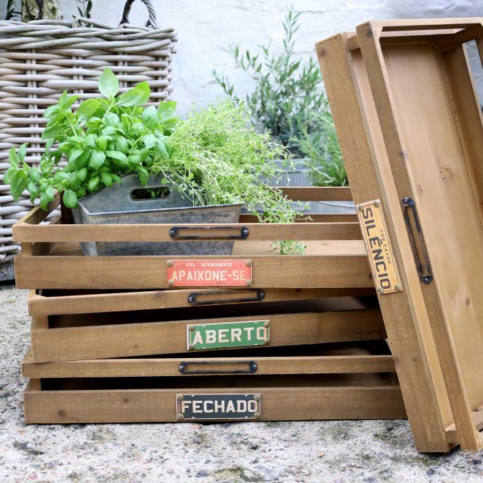 Stacked wooden storage crates with open slatted sides, metal handles, and decorative label plaques reading “Fechado,” “Silenc