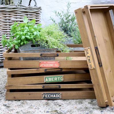 Stacked wooden storage crates with open slatted sides, metal handles, and decorative label plaques reading “Fechado,” “Silenc
