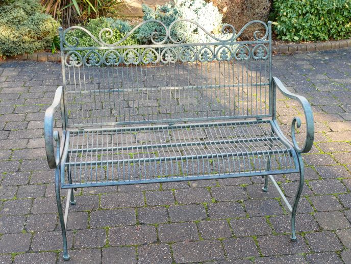 Wrought metal garden bench with decorative scrollwork and curved arms, finished in a soft vert patina