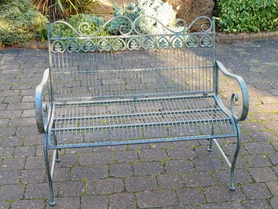 Wrought metal garden bench with decorative scrollwork and curved arms, finished in a soft vert patina