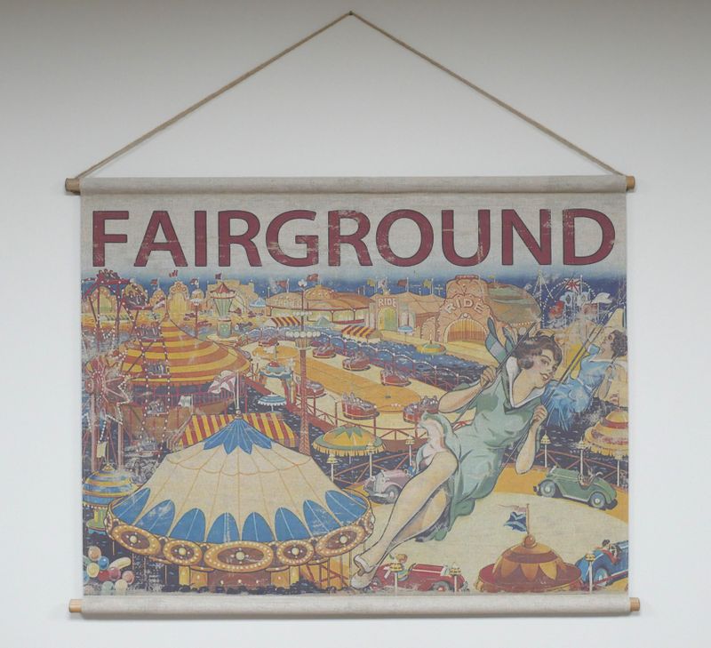 Fabric wall hanging showing a vintage fairground scene with rides, tents, and figures, topped with the word “FAIRGROUND”